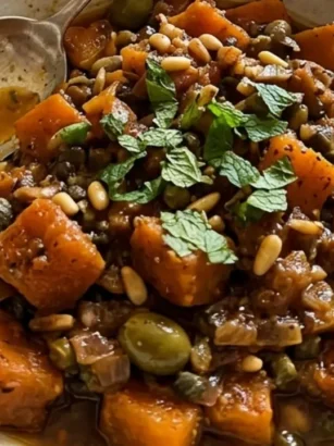 Foto di un piatto rustico con caponata di zucca rossa alla siciliana, guarnita con menta e pinoli, su un tavolo di legno antico.