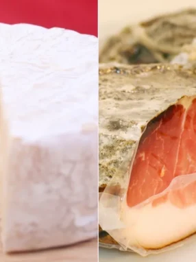 Primo piano di una forma di formaggio Brie tagliata e di un pezzo di speck stagionato.