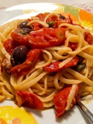 Piatto di linguine cremose mantecate con pomodorini, olive nere e capperi