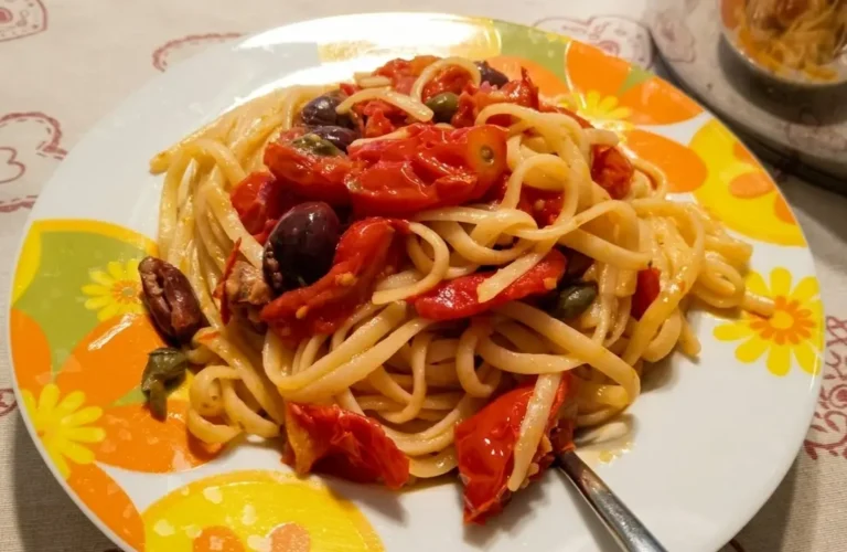 Piatto di linguine cremose mantecate con pomodorini, olive nere e capperi
