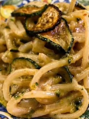 Piatto di Pasta alla Nerano originale mantecata con zucchine fritte e provolone su piatto di ceramica decorato
