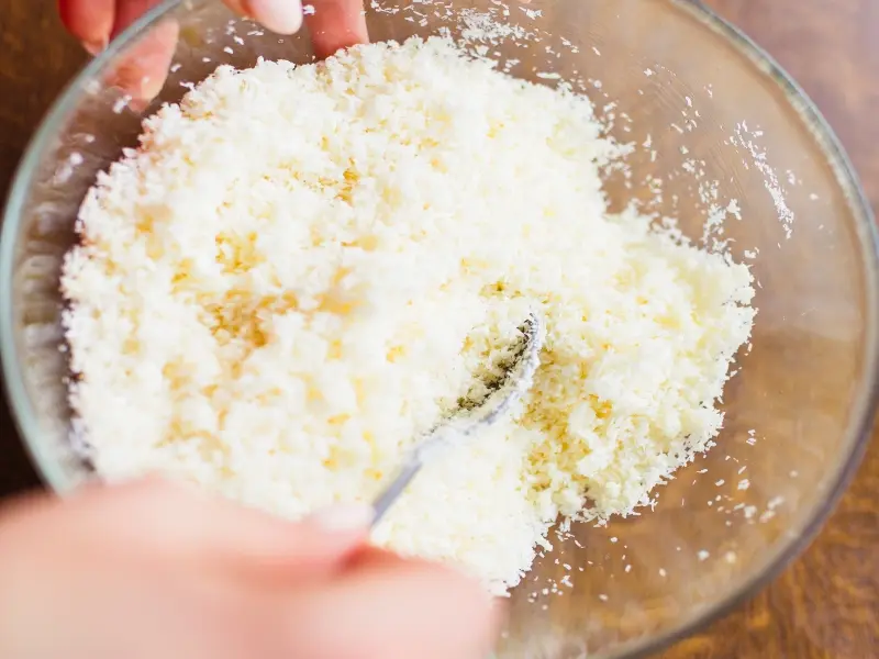 Mani che mescolano gli ingredienti in una ciotola di vetro su un tavolo di legno per la ricetta della lasagna di zucca e speck