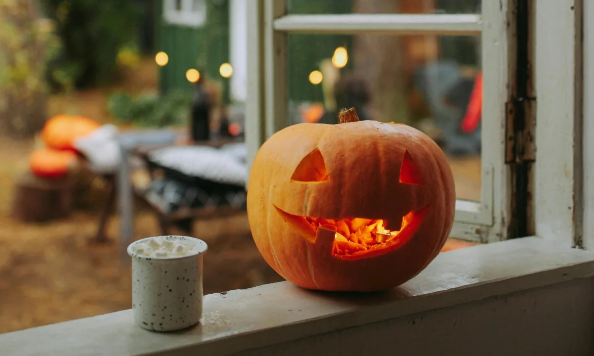 Zucca di Halloween illuminata dall'interno, intagliata con un sorriso e posta sul davanzale di una finestra con vista su un giardino sfocato.