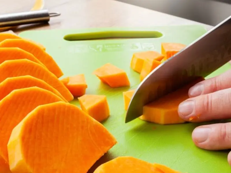 Tagliare la zucca a fette su un tagliere verde per preparare la lasagna di zucca e speck